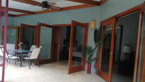 Ein geräumiges Zimmer mit Essbereich, Deckenventilator und Schiebegläsern zu einem anderen Raum.