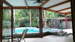 Ein überdachter Außenbereich mit Pool, Sitzgelegenheiten und Deckenventilator.