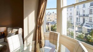 A room with a glass table and chairs, a sofa, and a view of buildings through a window. - Host & Stay | Havelock Place Apartment (Whitby)