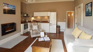 A living room with a fireplace, a dining area with a chandelier, and a kitchen with white cabinets. - Host & Stay | Havelock Place Apartment (Whitby)
