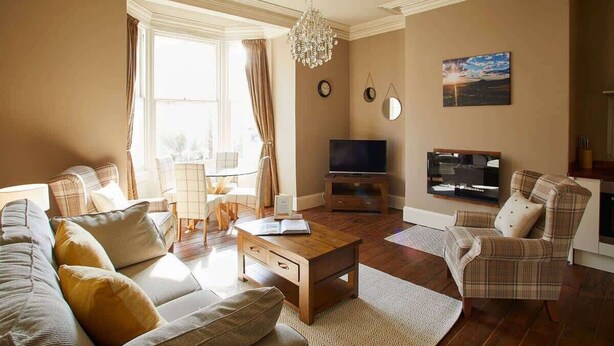 A living room with a sofa, armchairs, a coffee table, a TV, and a chandelier. - Host & Stay | Havelock Place Apartment (Whitby)
