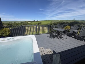 A deck with a hot tub, outdoor seating, and a view of the countryside.