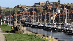 Um porto com barcos, uma estátua e edifícios históricos ao fundo.