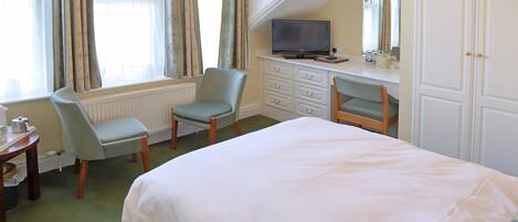 A hotel room with a bed, a desk with a television, a chair, and a dresser.