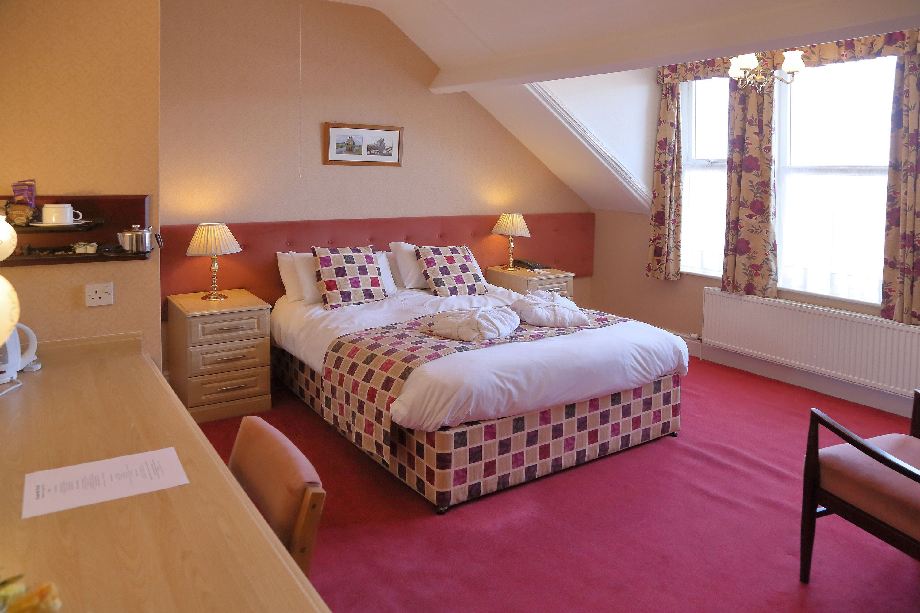 A bedroom with a checkered bedspread, two bedside lamps, a wooden desk, and a chair.
