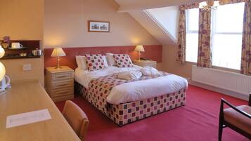 A bedroom with a checkered bedspread, two bedside lamps, a wooden desk, and a chair.