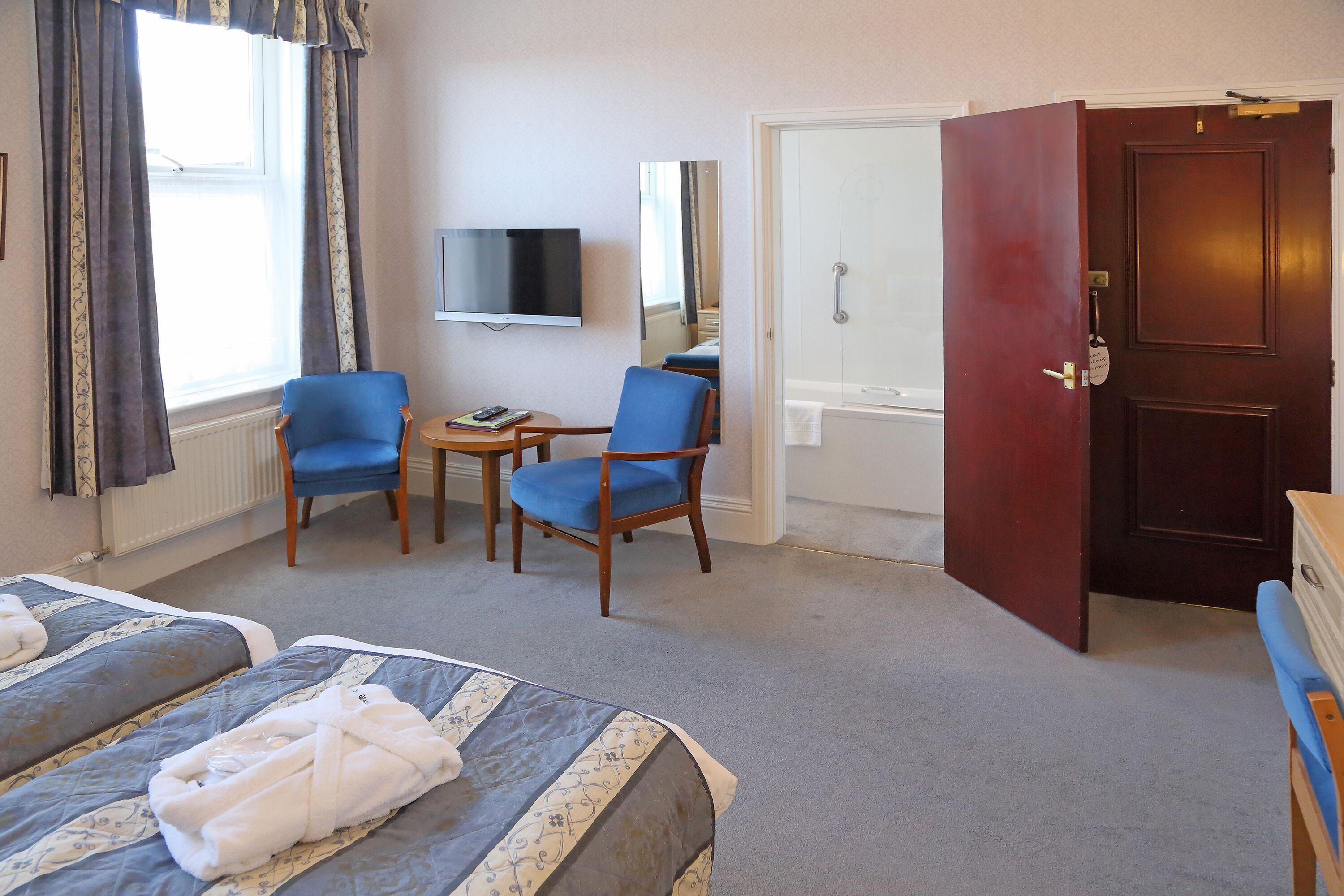 A hotel room with two beds, a TV, a small table, two chairs, and a door leading to a bathroom.