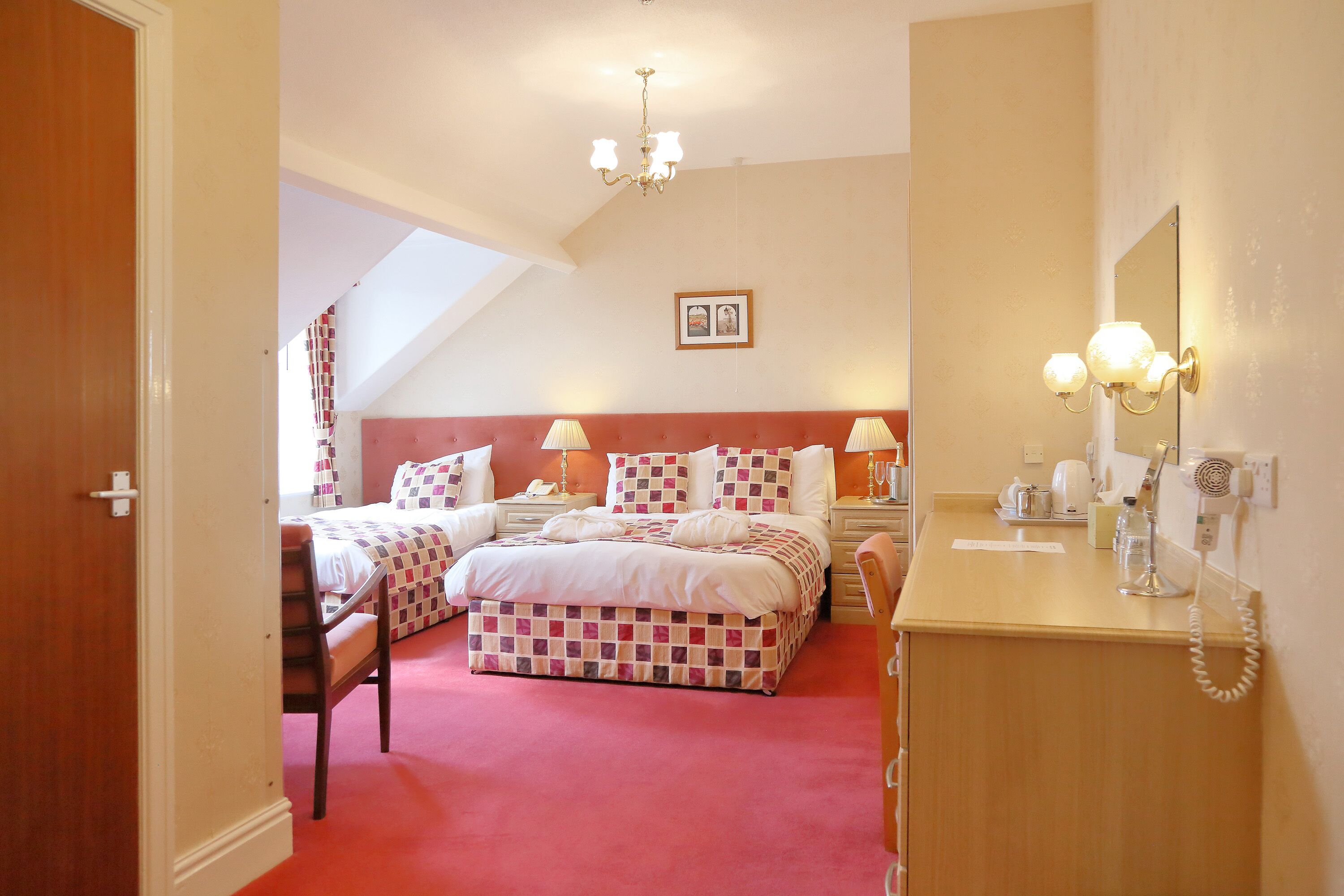 A bedroom with two beds, a wooden dresser, a mirror, and a chandelier.