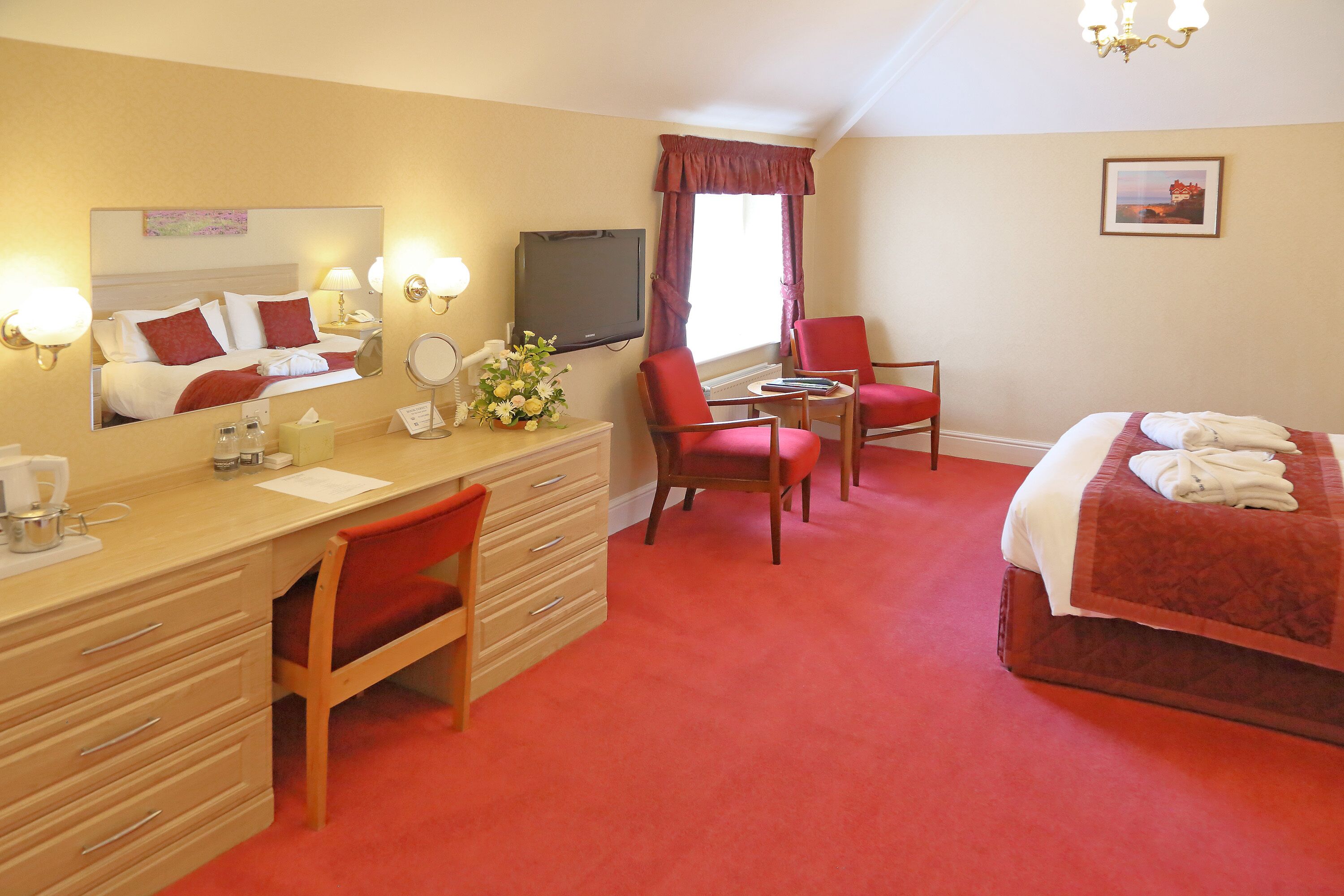 A hotel room with a bed, a desk with a chair, a TV, and a window with curtains.