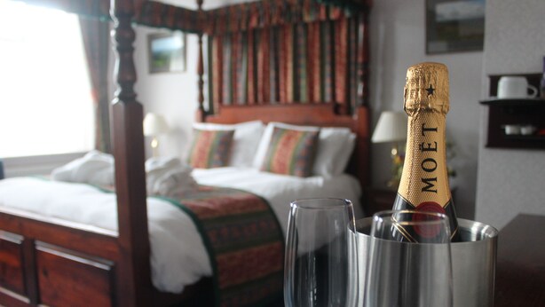 Uma cama com cabeceira de madeira, mesa de cabeceira com uma garrafa de champanhe Moët e um copo.