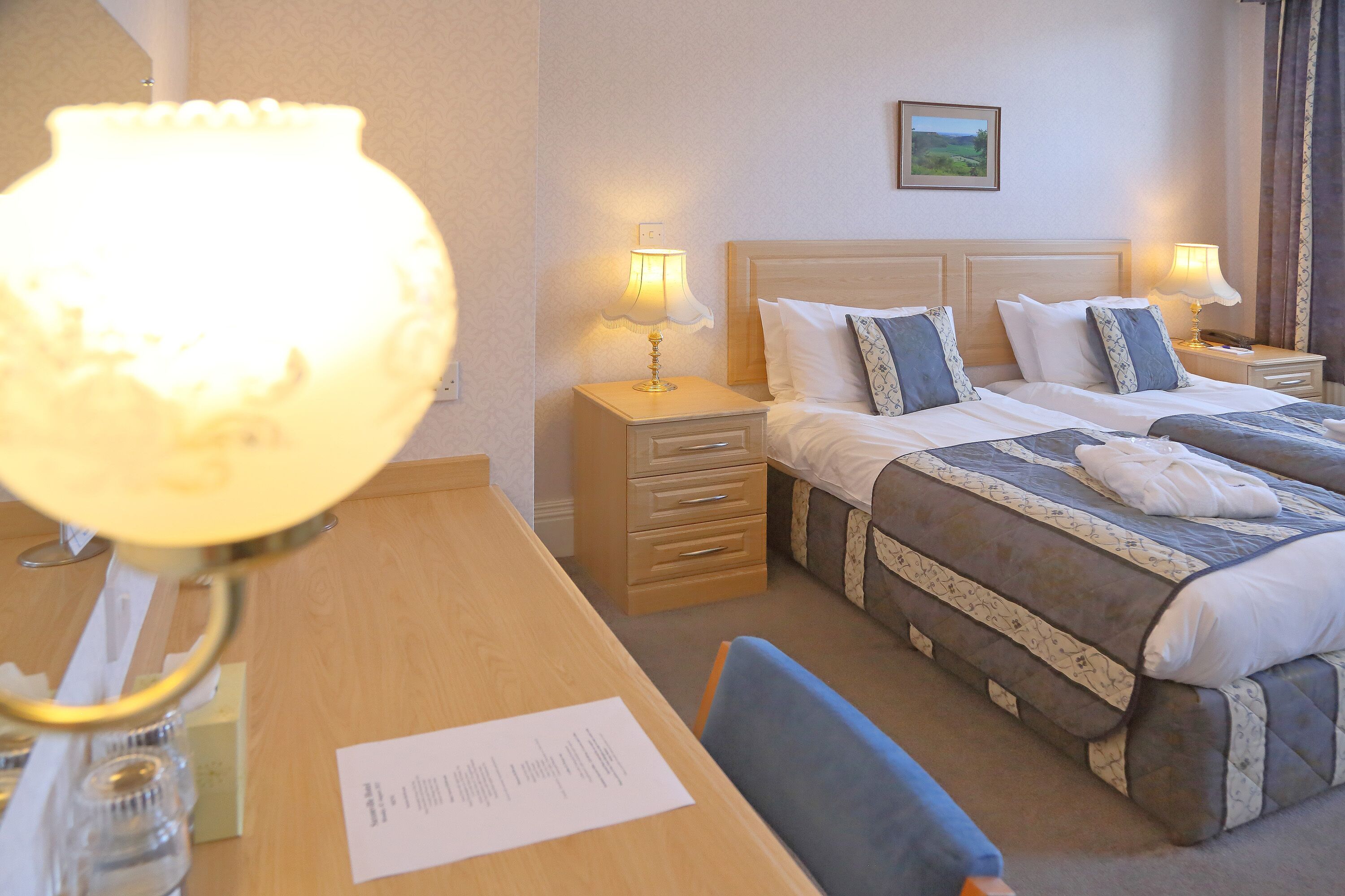 A hotel room with a double bed, two bedside tables with lamps, a wooden desk, and a chair.