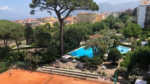 Un court de tennis avec une piscine et de la verdure tout autour.