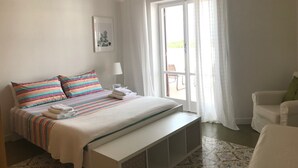 Une chambre à coucher avec un lit, un banc, une chaise, une lampe et une vue sur l’extérieur.