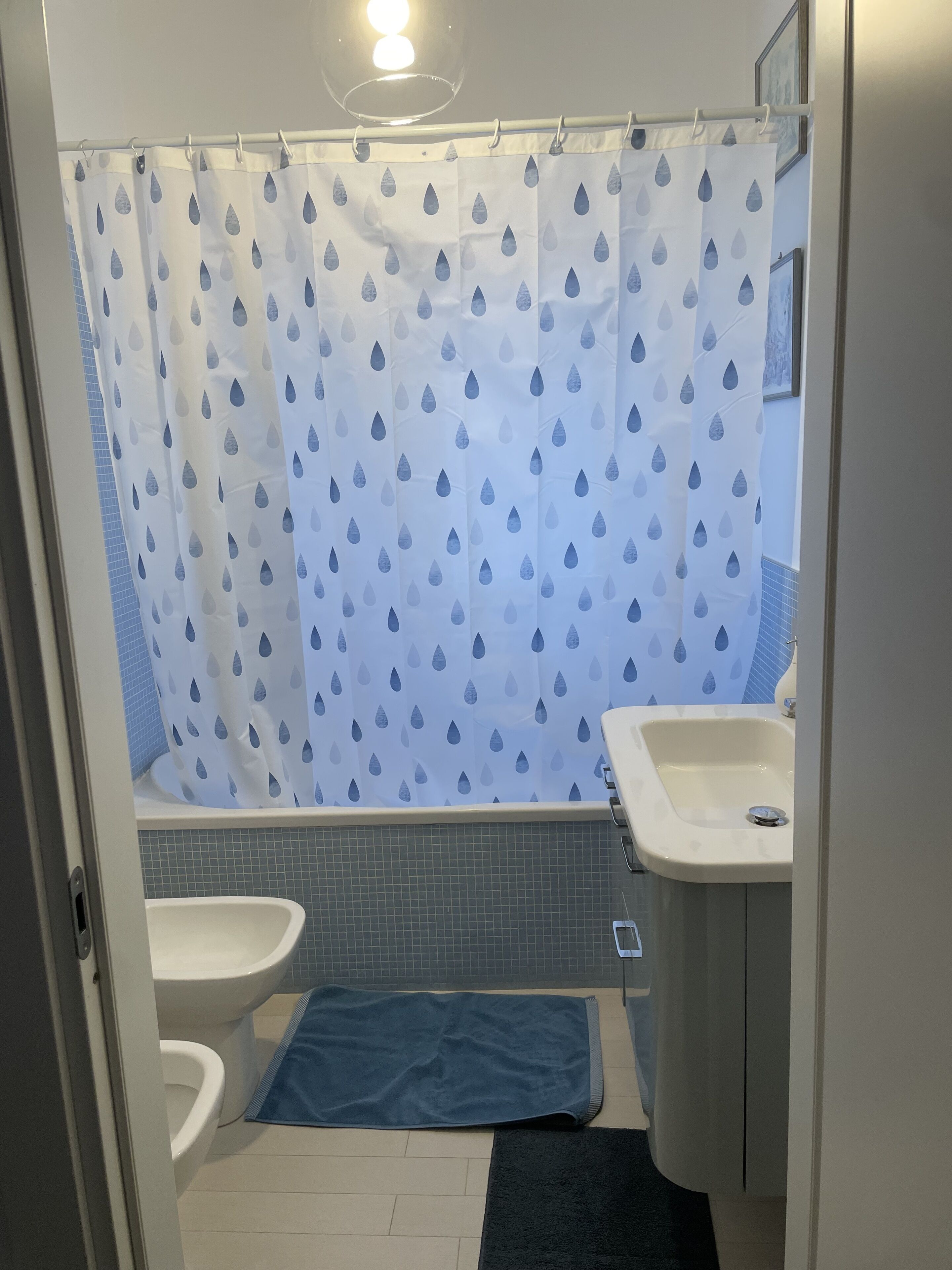 A bathroom with a shower curtain, a sink, a toilet, and a blue towel on the floor.