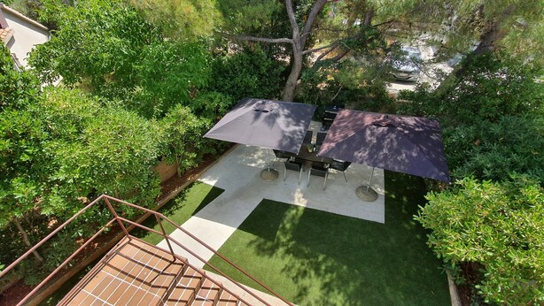 Une terrasse extérieure avec une table et des chaises, protégée par deux parasols, et entourée d’une végétation luxuriante.