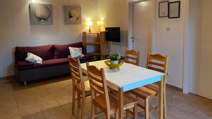 Un salon chaleureux avec un plafond en bois, un canapé rouge, une table blanche avec des chaises et un téléviseur fixé au mur.
