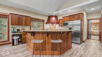 Una cocina con armarios de madera, un refrigerador de acero inoxidable, un microondas y una isla grande con taburetes de bar.