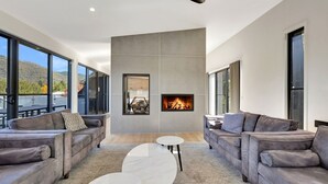 A modern living room with a fireplace, large windows, and grey sofas.