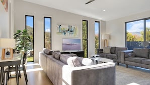A modern living room with a large flat-screen TV, grey sofas, and a dining area with a glass table.