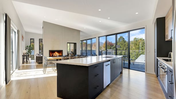 A modern kitchen with a large island, a fireplace, and large windows offering a view of the outdoors.