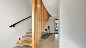 A modern staircase with wooden steps and a black handrail, leading to a door with a view of a parking area.