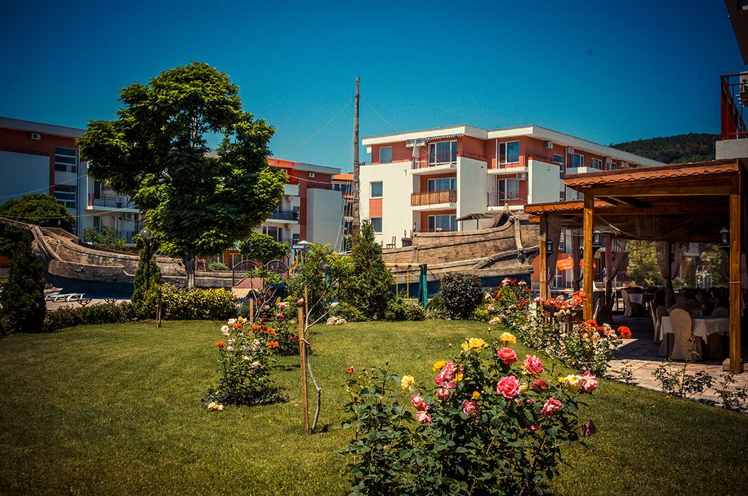 Un patio de hotel con césped, macizos de flores y un área de comedor al aire libre techada.