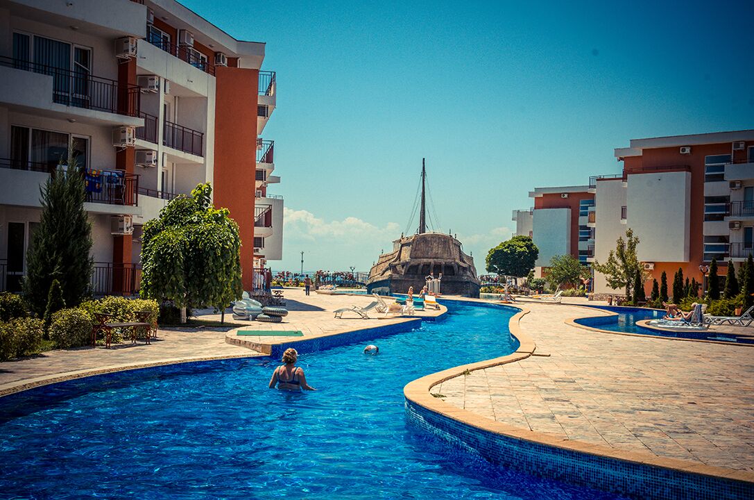 Un espace piscine agrémenté d’un rocher central, entouré d’immeubles à plusieurs étages dotés de balcons.