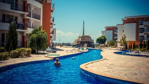A swimming pool area with a central rock feature, surrounded by multi-story buildings with balconies.