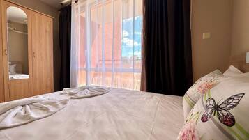 A bedroom with a large window, a wooden wardrobe, and a bed with floral bedding.