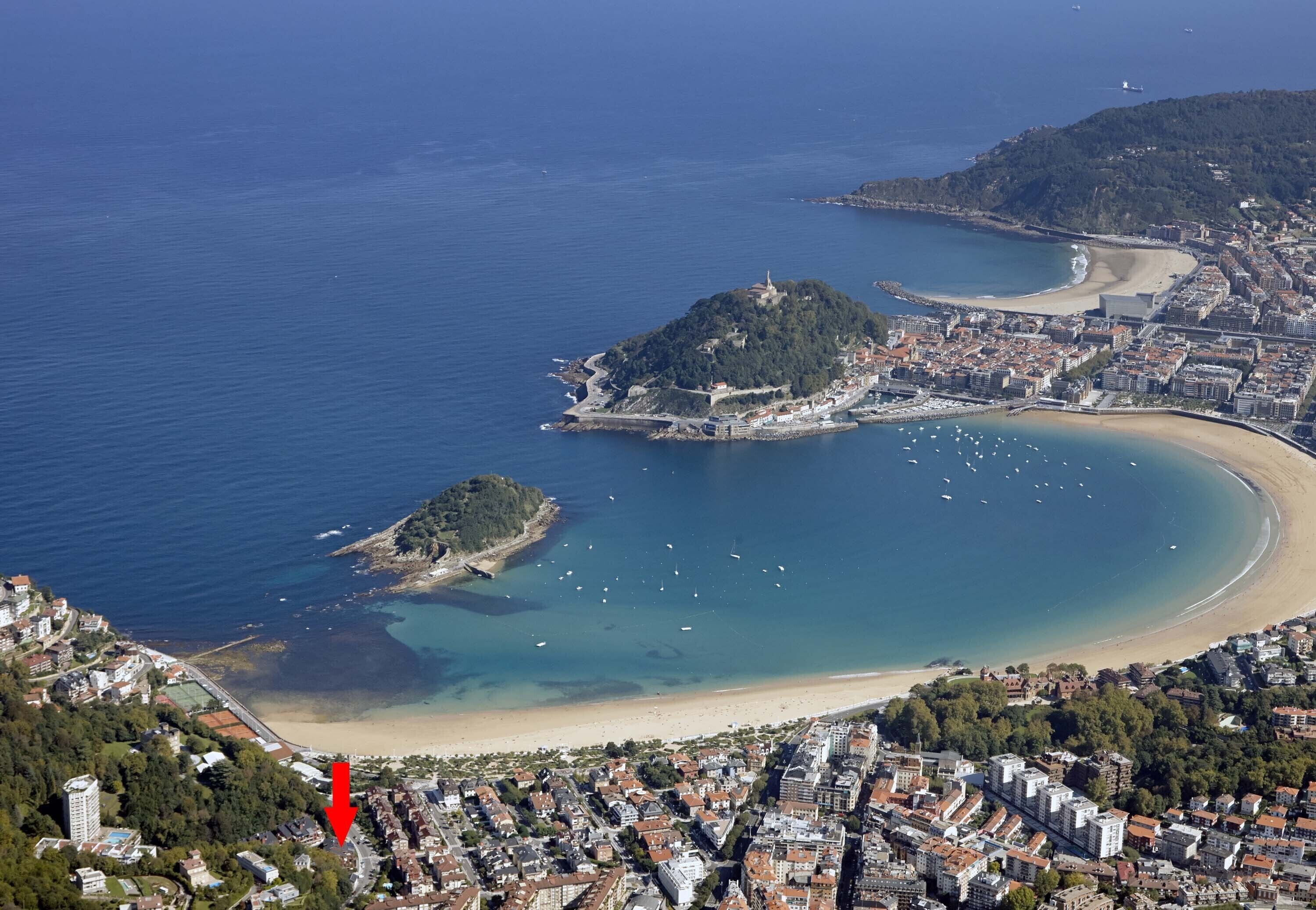 Vue aérienne d’une ville côtière, avec une colline imposante, une plage et un port de plaisance.