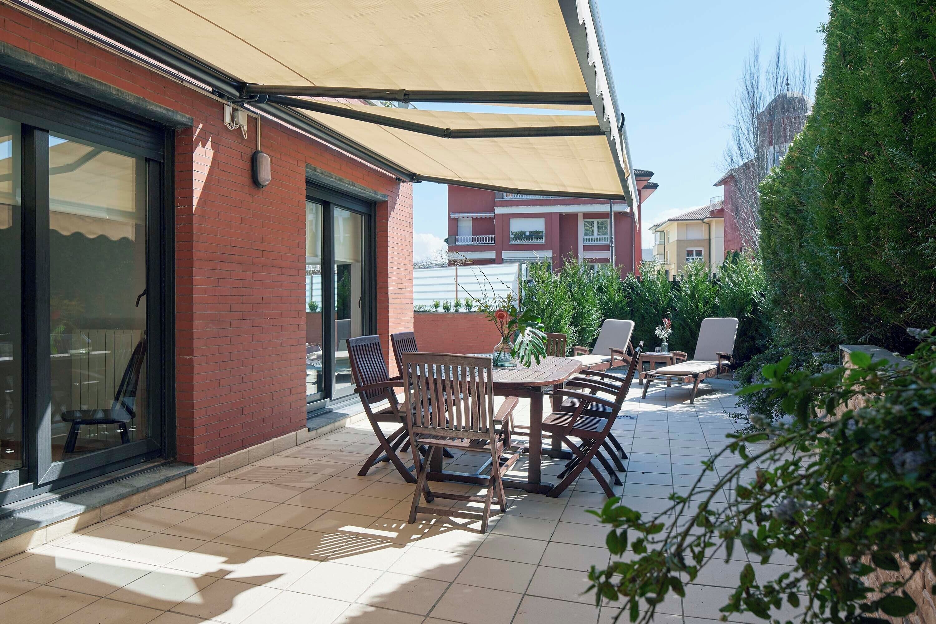 Een terras met een tafel en stoelen, een overdekt gedeelte en een bakstenen muur.