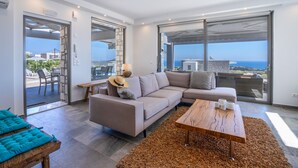 Una sala moderna con un sofá, una mesa de centro de madera y vistas al mar a través de amplios ventanales.