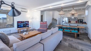 Una sala de estar moderna con un sofá, una mesa de centro y un televisor. Hay una zona de cocina con una mesa de comedor y bancos.