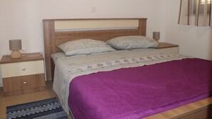 A bedroom with a wooden headboard, a purple bedspread, two bedside tables with lamps, and a patterned rug. - Apartman Gracijela Poreč (Parenzo)