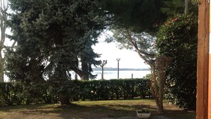 A stone-paved courtyard with a large tree, a hedge, and a view of the water. - Alla Ghigliotta holiday home (Viverone)