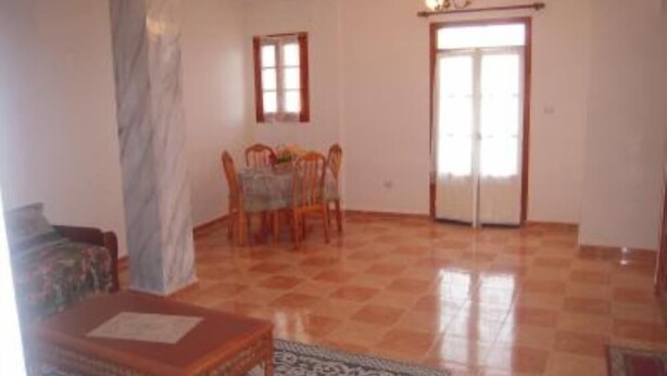 Amplia habitación con piso de baldosas, una mesa de comedor con sillas, una araña y un ventanal corredero.