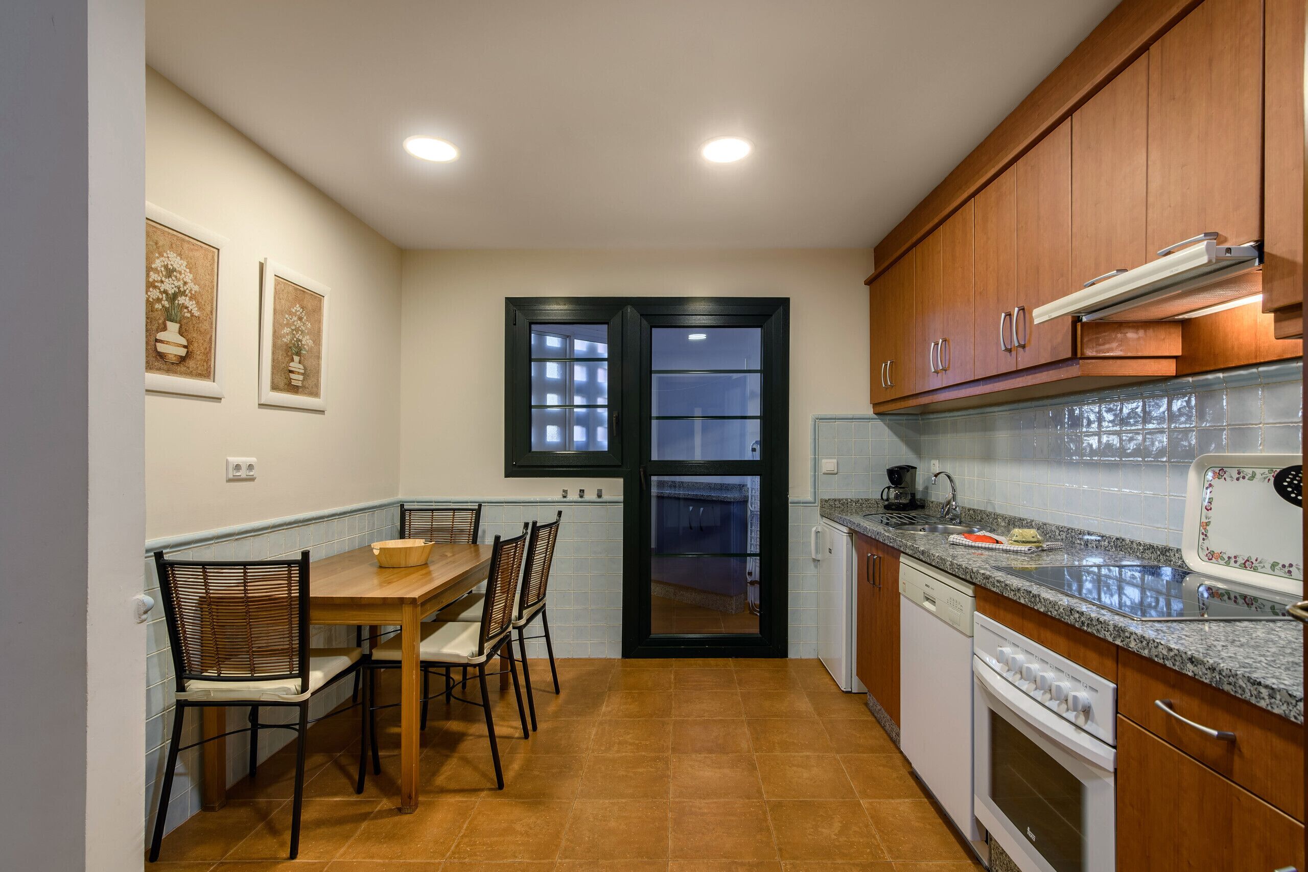 Cocina funcional con armarios de madera, una mesa de comedor con sillas, horno empotrado y ventana con vistas.