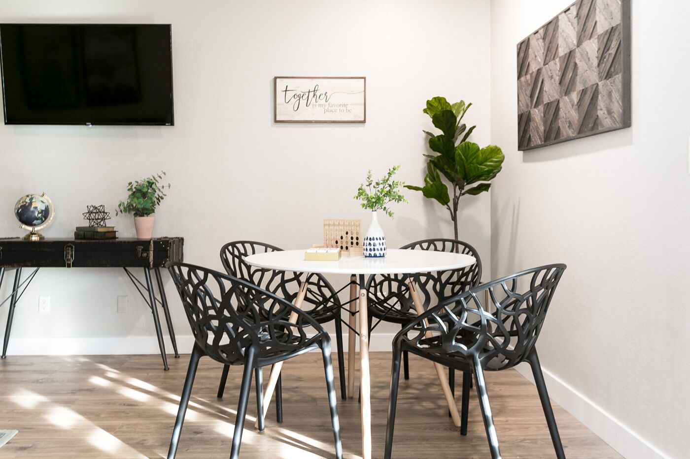 A dining area with a round table, black chairs, a globe, books, and a plant on a console table.