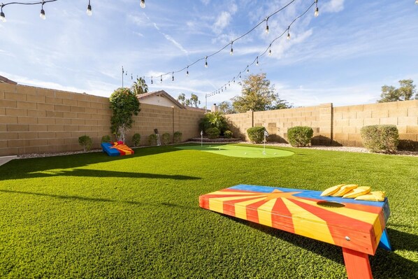 A backyard with artificial grass, a colorful play structure, and string lights. - Gilbert Oasis | Pool, Putting Green, Sleeps 10 (Gilbert)