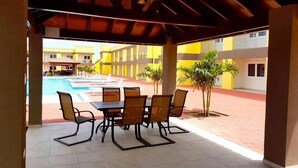 An outdoor patio with a pool, surrounded by yellow buildings, featuring a table and chairs. - Casa Alessandra 2bdr (Oranjestad-West)