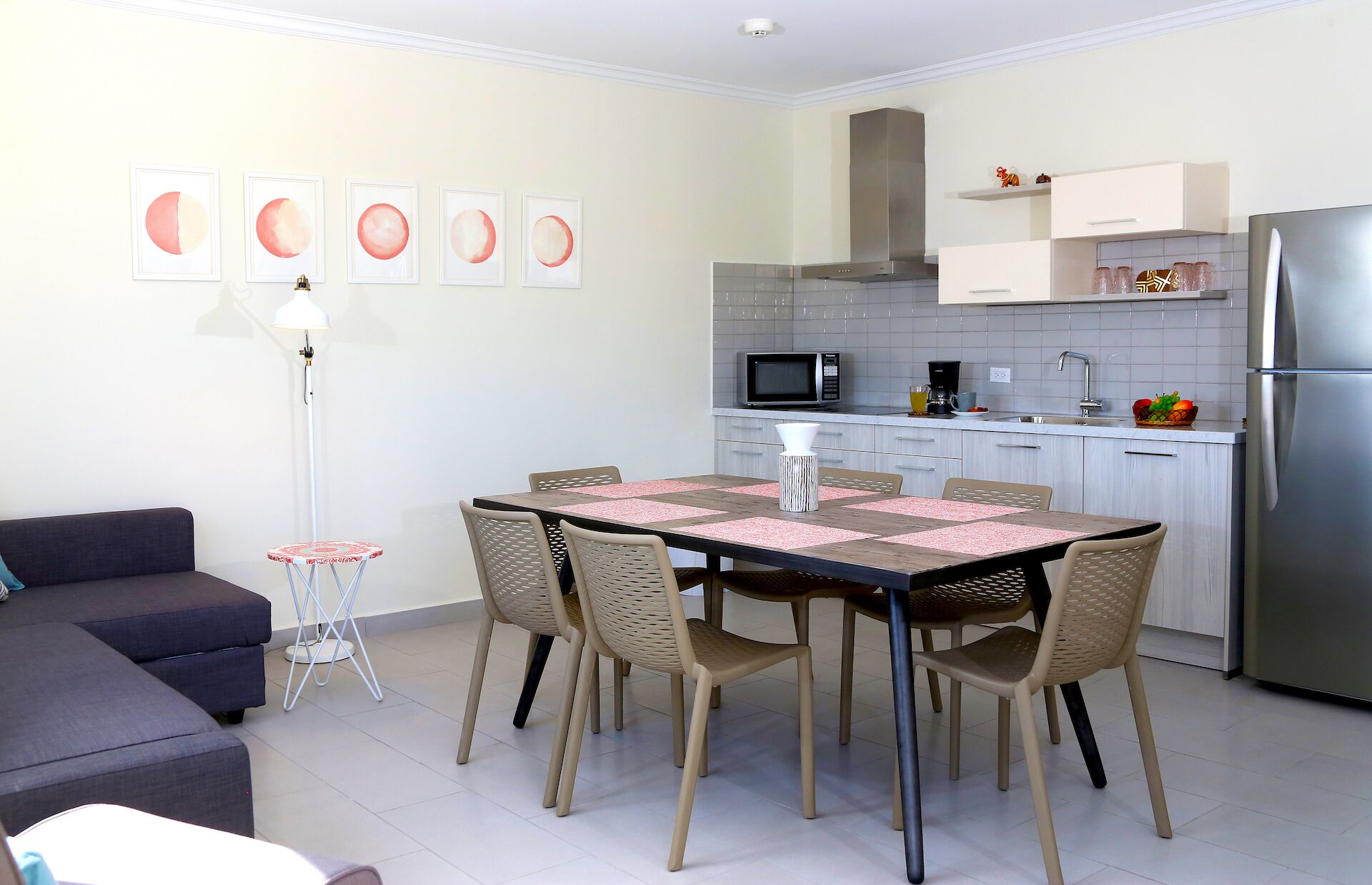 A modern kitchen with white cabinets, a stainless steel refrigerator, and a dining area with a table and chairs.