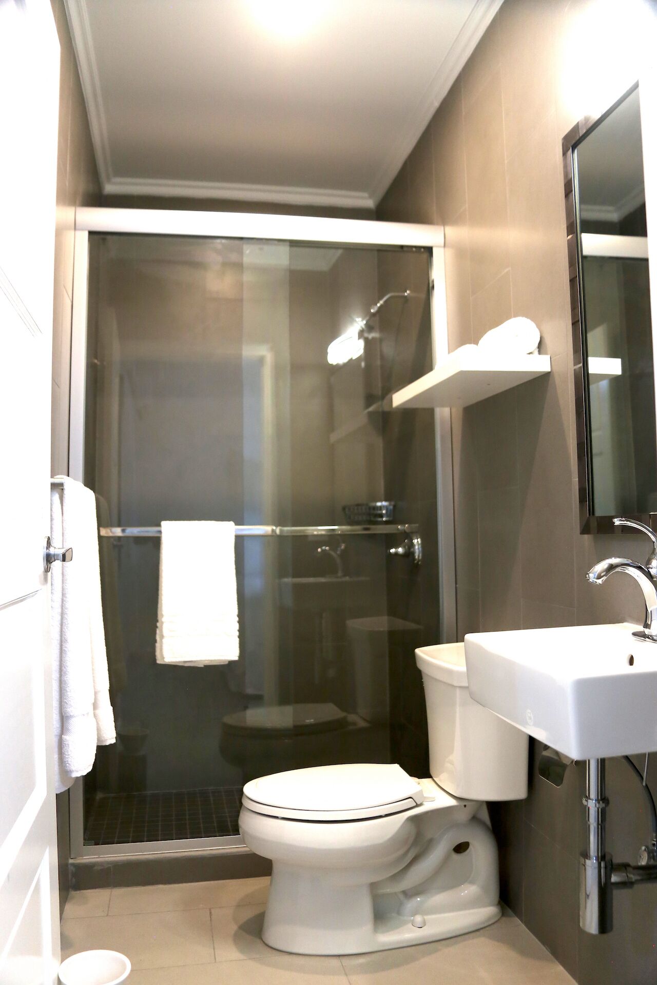 Un baño moderno con ducha envuelta en vidrio, inodoro blanco y lavamanos con espejo superior.