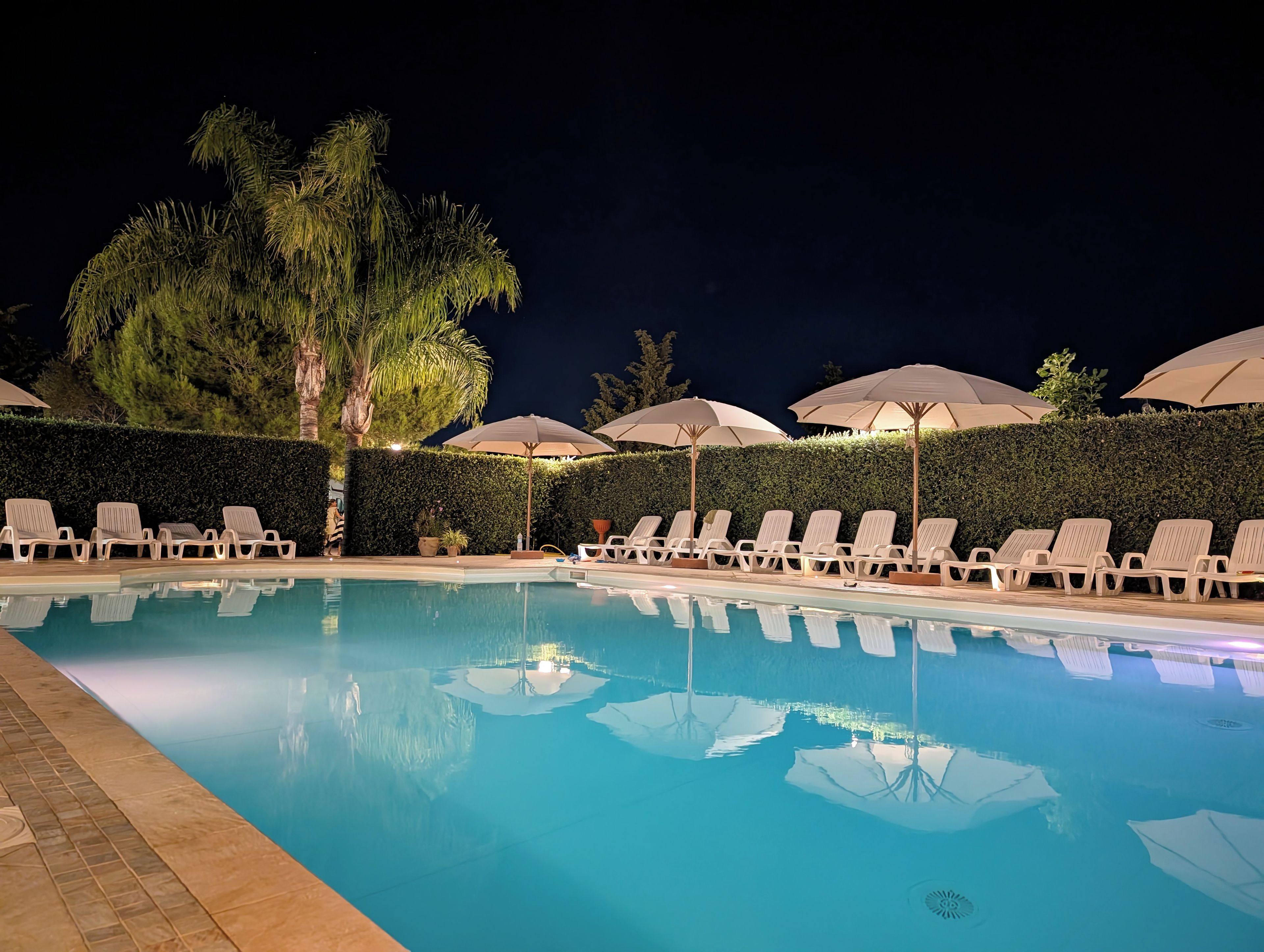 Uma área de piscina à noite, com espreguiçadeiras e guarda-sóis.