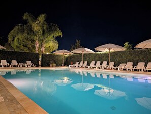 Un espace piscine aménagé pour la nuit, avec des chaises longues et des parasols.