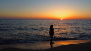 Una persona de pie en la playa al atardecer.