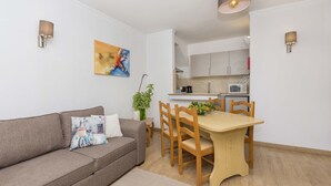 A modern living room with a sofa, a dining table with chairs, a kitchen in the background, and a painting on the wall. - Apartment Maresia, 50 metres from the Oura Beach and 2 minutes from the Strip (Albufeira)