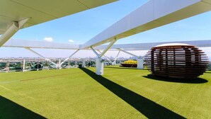 A rooftop terrace with a clear view of the city skyline, a large wooden sculpture, and a well-maintained lawn. - Azure Tropical Paradise in your Backyard (Parañaque)
