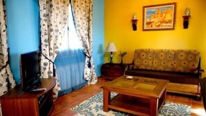 A living room with a sofa, a coffee table, a TV on a stand, patterned curtains, and a wall-mounted lamp. - RURAL HOUSE FOR 2 PEOPLE IN TUREGANO (Turégano)
