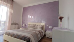 Quarto com cama, mesas de cabeceira, cómoda e janela com cortinas.