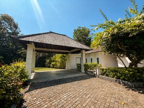 A covered entrance with a tiled roof, a paved driveway, and lush greenery.
